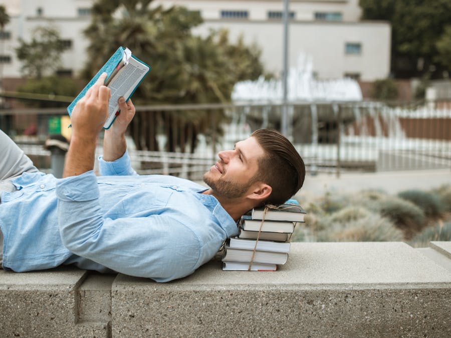 A man relaxes reading a book outdoors on a concrete bench, enjoying a sunny day.