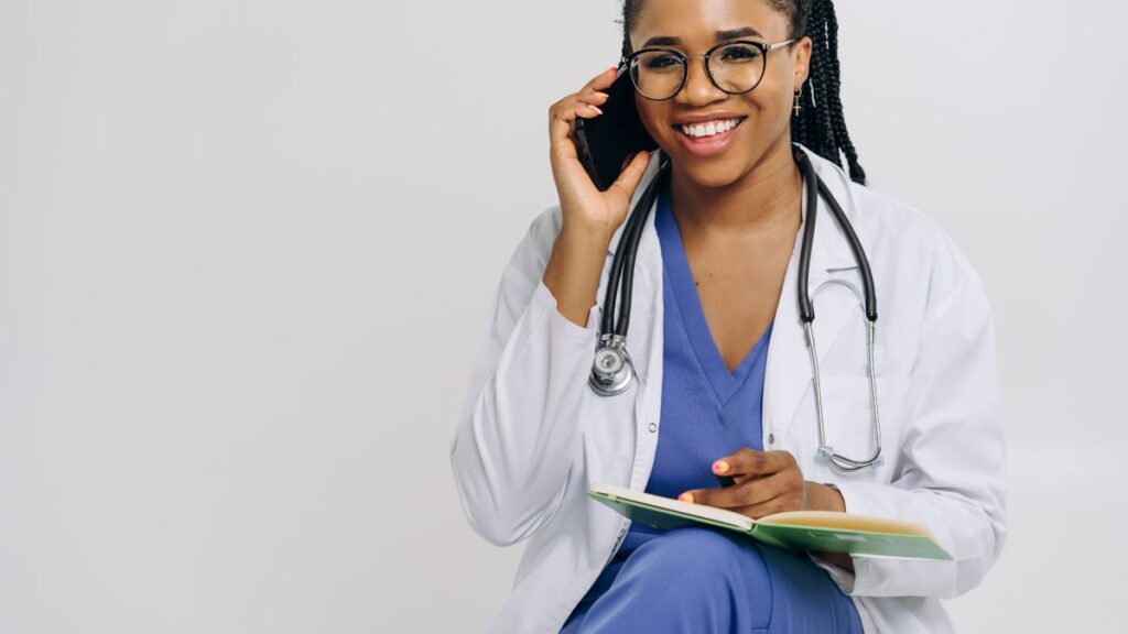 Cheerful female doctor in lab coat talking on smartphone and taking notes.