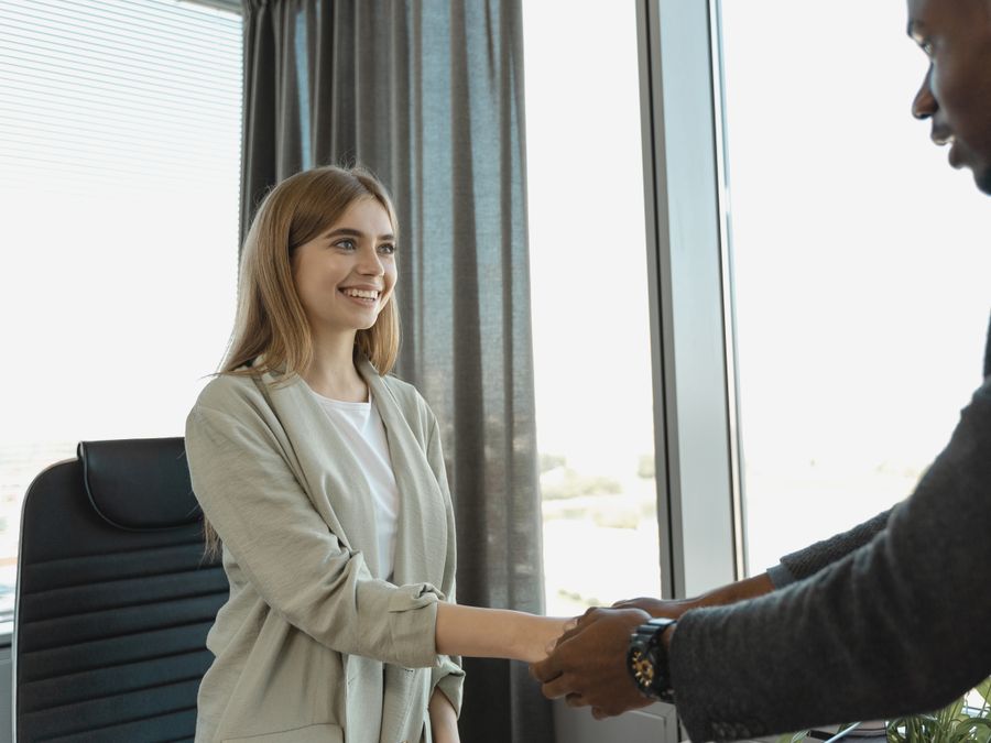 Woman smiling and shaking hands at a business office, signaling a successful job interview.