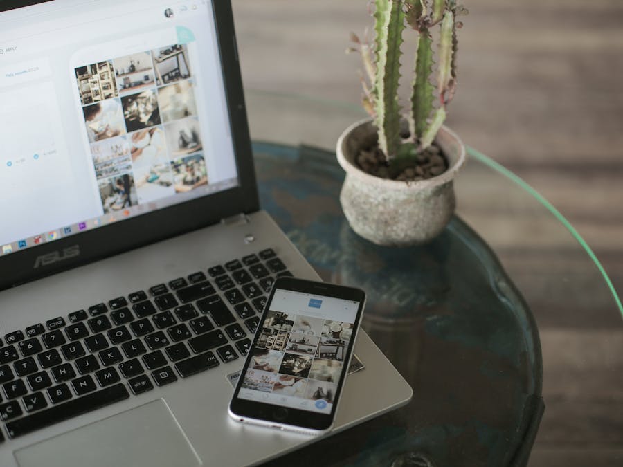 A laptop and smartphone displaying social media apps next to a cactus on a glass table.