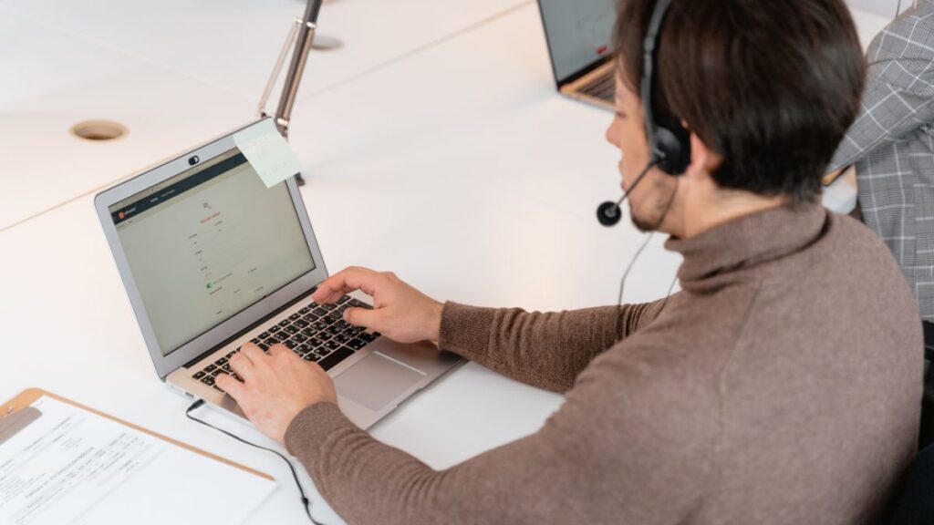 Call center agent wearing headphones working on a laptop in a modern office setting.