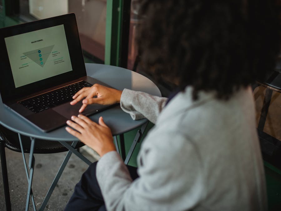 Back view of anonymous ethnic female in suit working with chart on computer while sitting at table in outdoor cafe during remote work