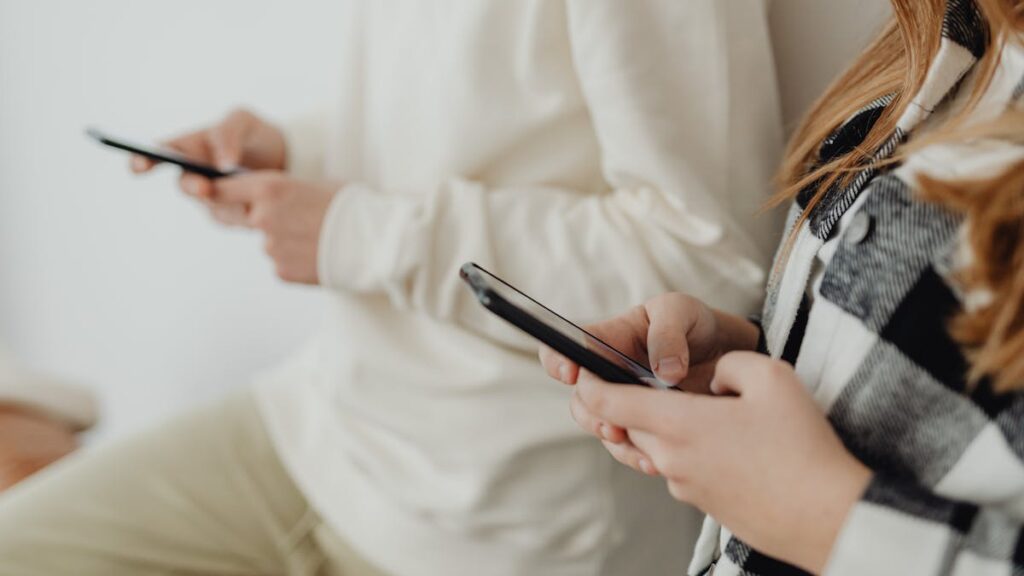 Close-up of two people using smartphones indoors, highlighting technology and communication.