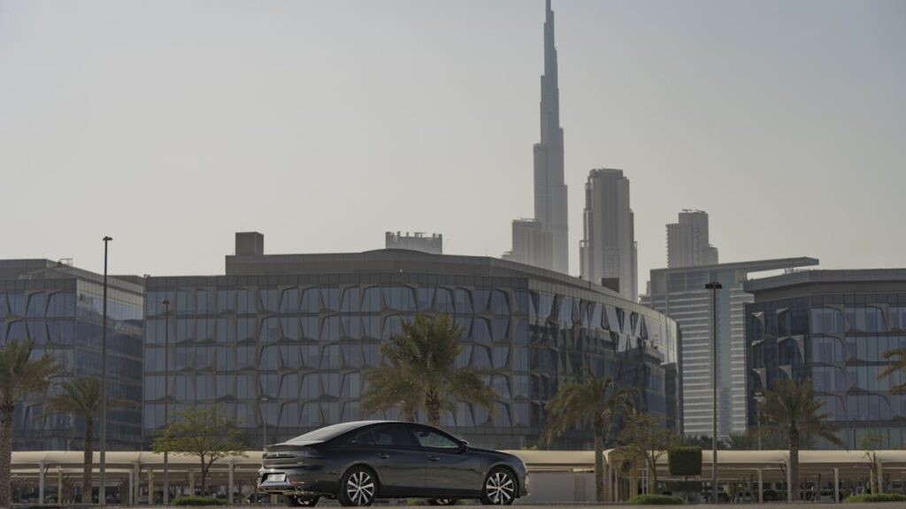 A car parked with a backdrop of Dubai's cityscape and Burj Khalifa under clear skies.