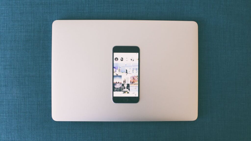 Flat lay of a smartphone on a laptop with social media photos on screen.