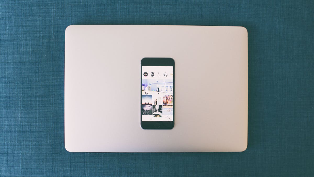 Flat lay of a smartphone on a laptop with social media photos on screen.