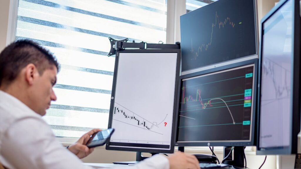 A stock trader analyzes financial data on multiple computer screens in an office setting.