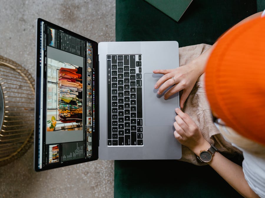 Person wearing orange beanie editing photos on laptop using professional software.
