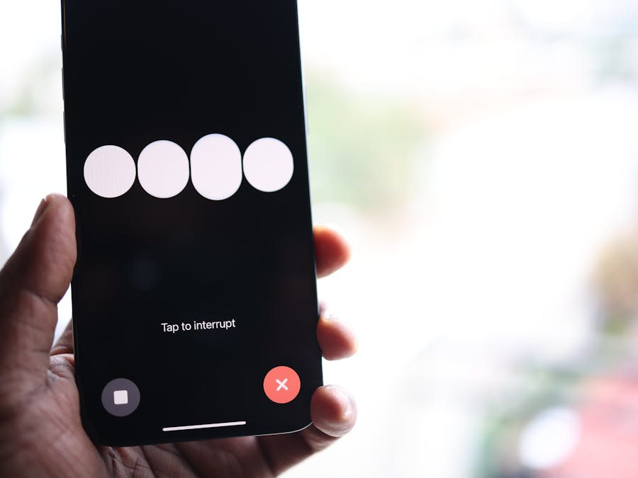 Close-up of a smartphone screen displaying a 'Tap to interrupt' prompt held in a hand.