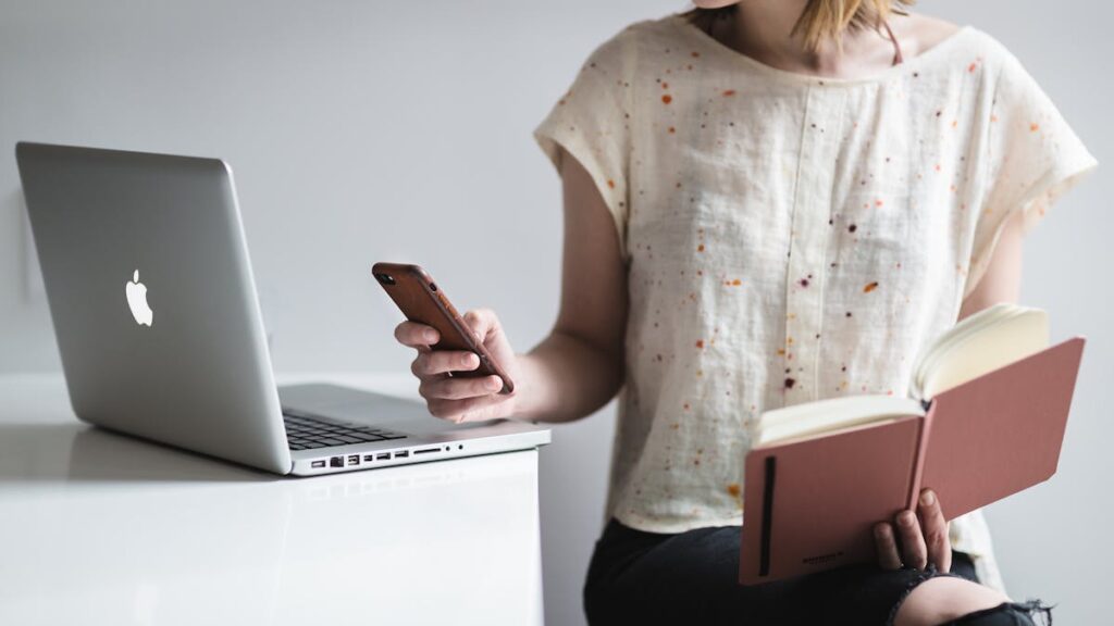 Woman working on a laptop while reading and texting, embodying modern multitasking.