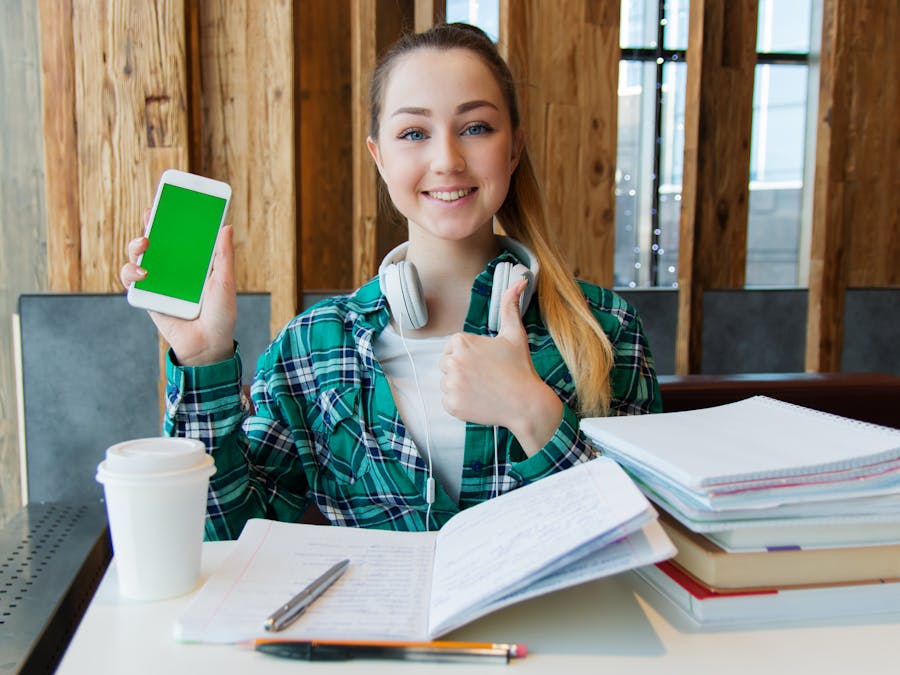 Smiling young woman using a smartphone while studying with books, showcasing modern education.