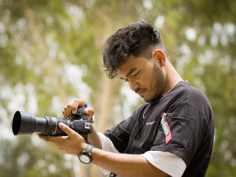 A young male photographer setting up his camera outdoors, focused and ready to capture the moment.