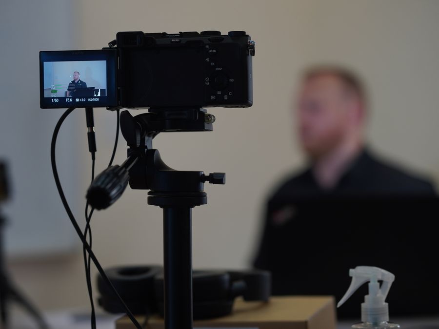 Close-up of camera setup during an indoor filming session with a blurred speaker in the background.