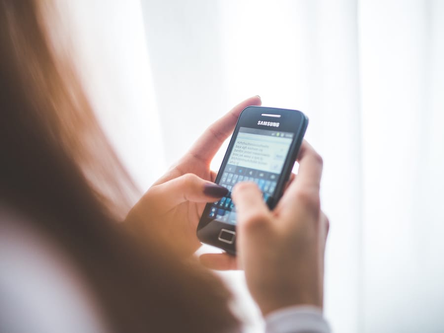 Close-up of a young woman typing on a Samsung smartphone at home. Bright indoor lighting.