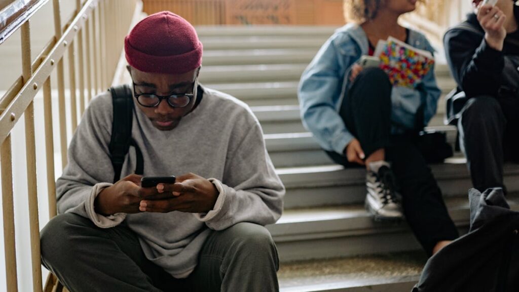 Group of young adults sitting on stairs, engaged with smartphones while relaxing indoors.