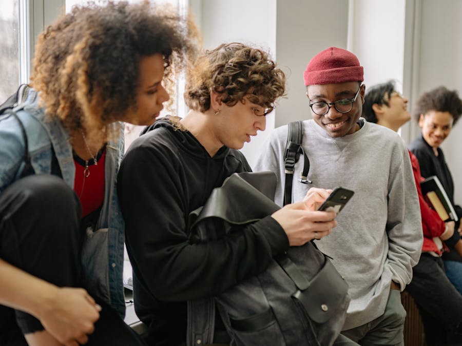 A group of diverse college students hanging out indoors and using a smartphone together.