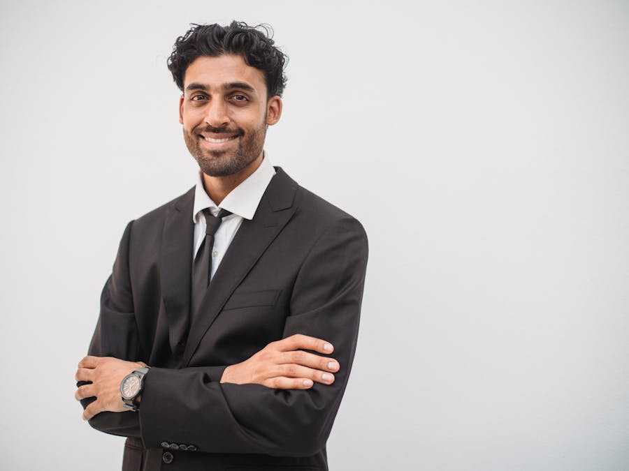Young businessman in a black suit smiling confidently against a white background.