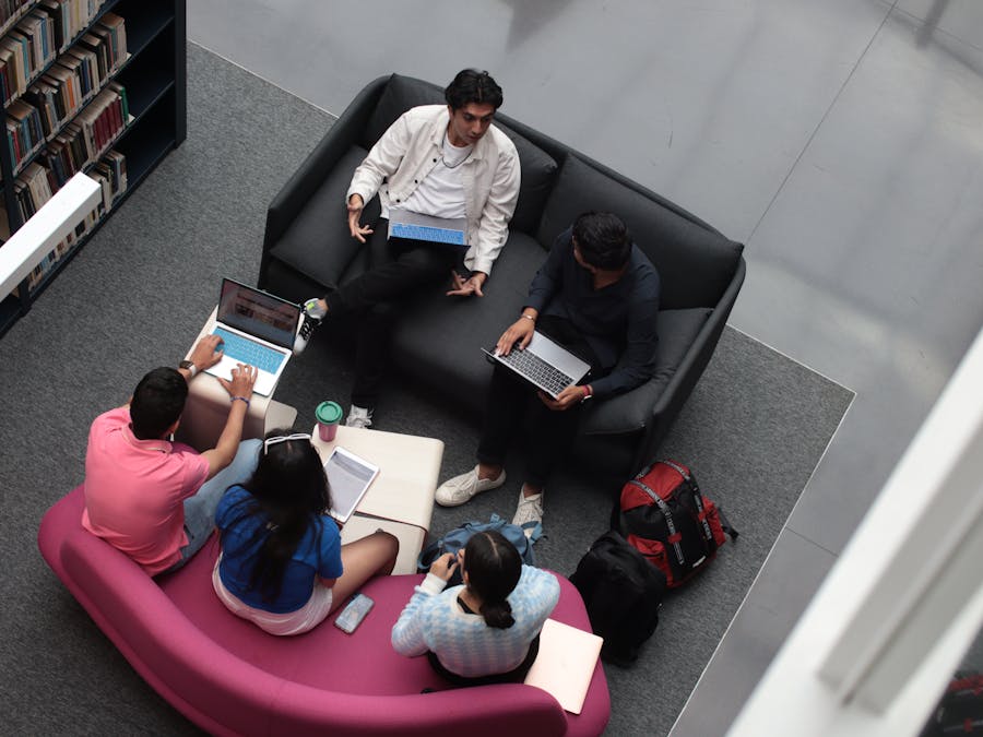 A group of diverse students using laptops and books in a library setting, studying together.