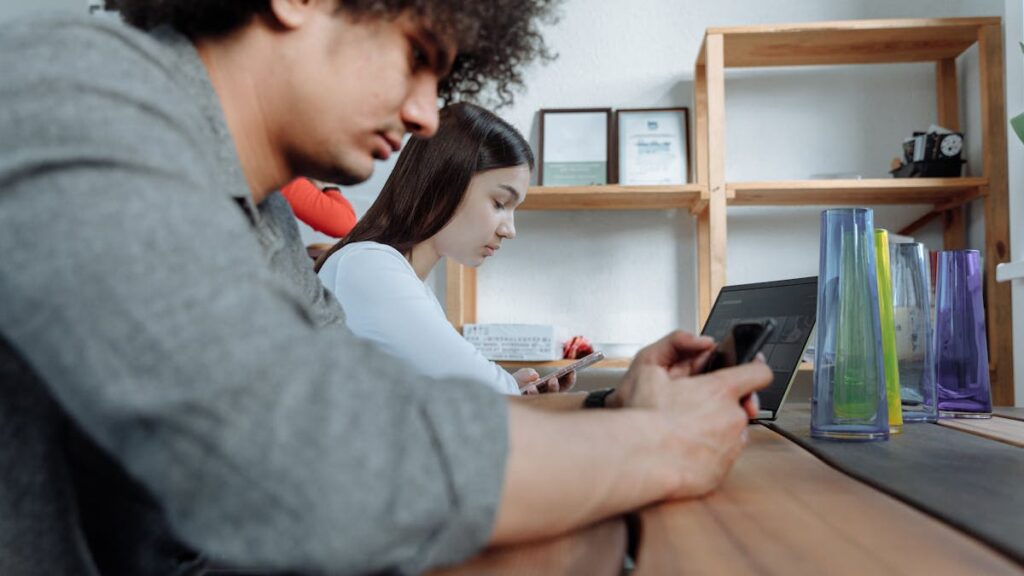 Students focused on smartphones and laptops in a modern classroom setting.