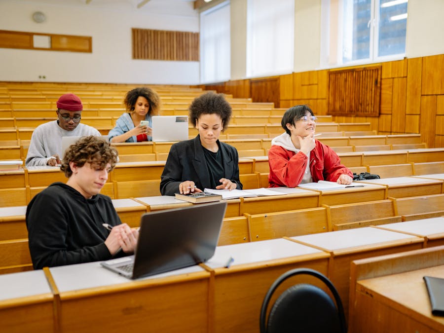 Group of college students studying together in a classroom, focused on learning with laptops and books.