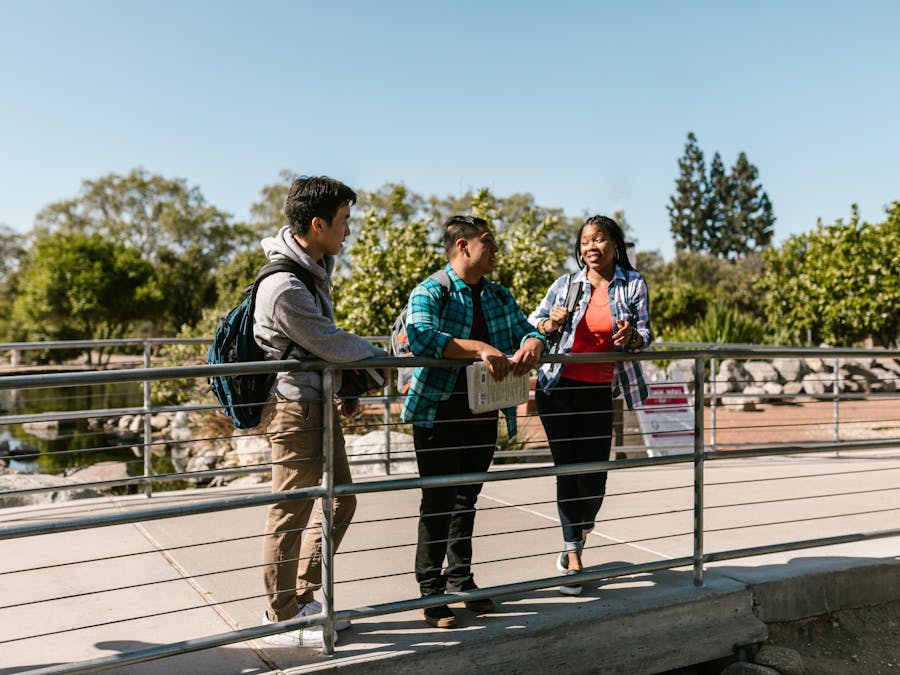 Three college students enjoying a conversation on a sunny day on campus bridge.