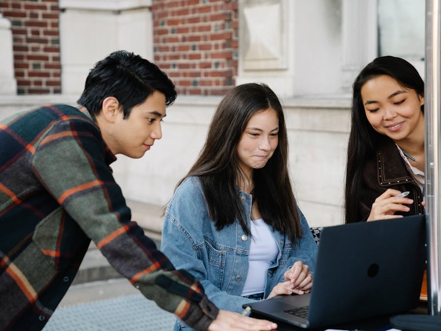 Diverse group of college students studying outdoors with a laptop, fostering collaboration.