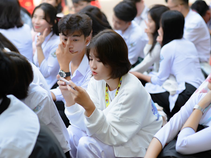 Group of students sitting outdoors, using smartphones and engaging with technology.