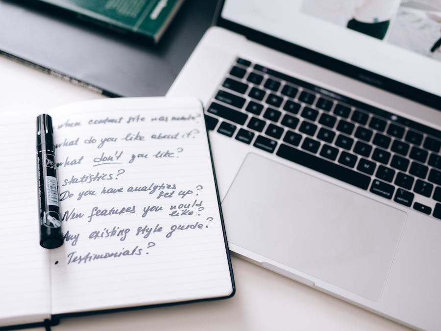 A notebook with handwritten notes next to a laptop on a workspace desk.