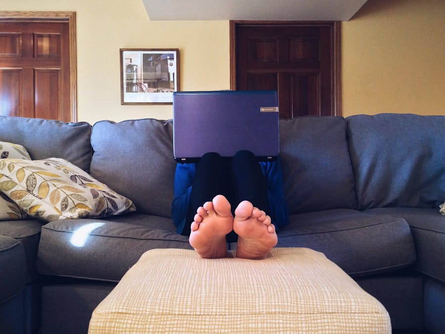 Person relaxing on a cozy couch with a laptop, embodying modern home comfort.