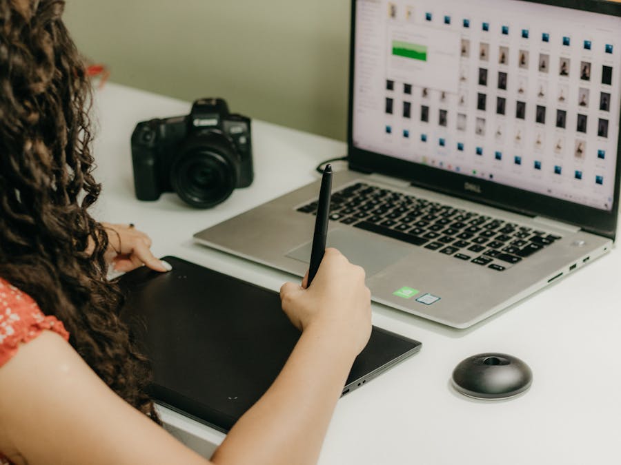 A woman using a graphics tablet and laptop, reviewing photos. Ideal for creative workspace themes.