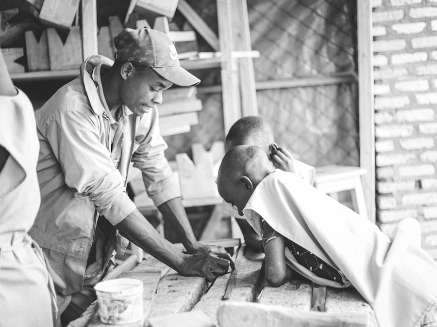 A mentor guides young boys in a carpentry workshop, fostering skill and curiosity in woodworking.