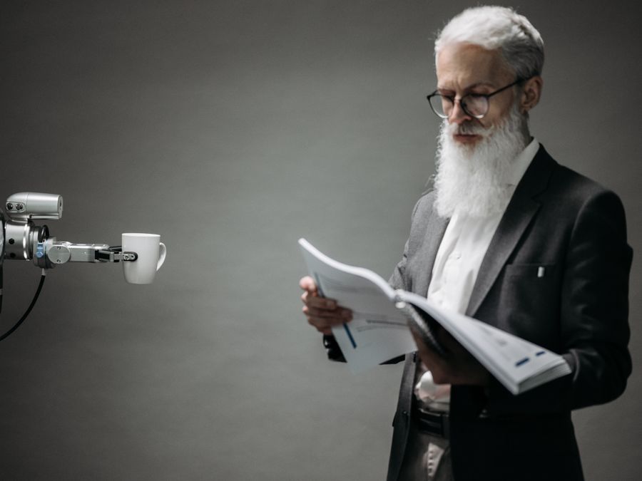 A robot arm assists a professional with a book and coffee in a modern office setup. Technology meets innovation.