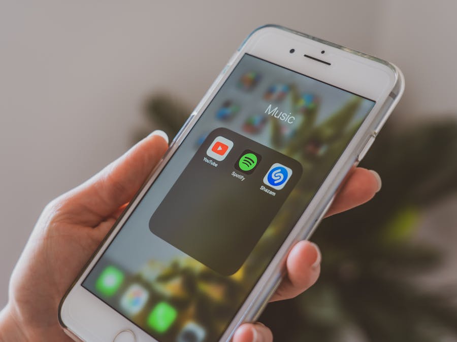 Hand holding a smartphone displaying popular music apps like Spotify and Shazam in a close-up shot.