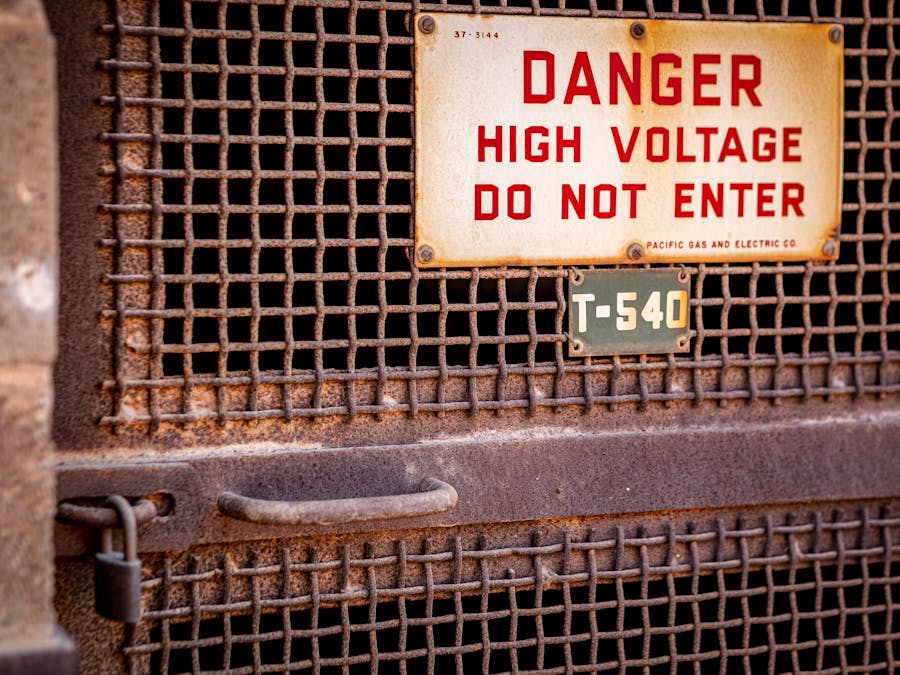 Close-up of a rusty industrial gate with a high voltage warning sign, conveying danger.