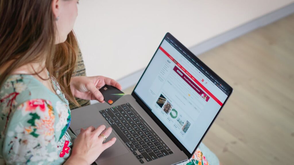 Woman in floral dress shopping online with a laptop and credit card indoors.