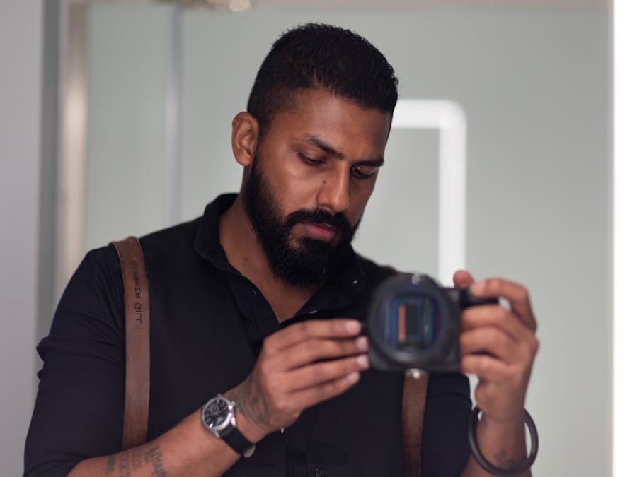 A bearded man concentrates on his camera in an indoor setting, showcasing focus and dedication.