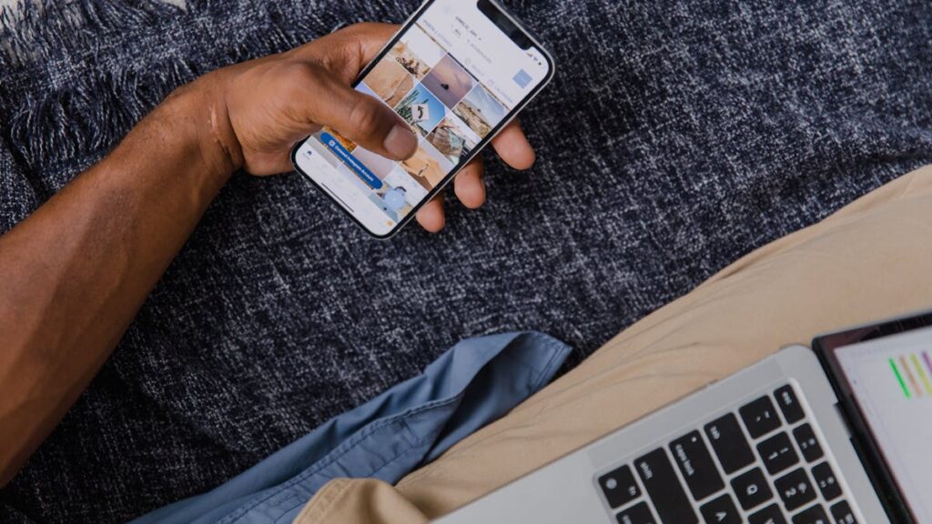 Hand holding smartphone with open laptop, showcasing modern digital lifestyle.
