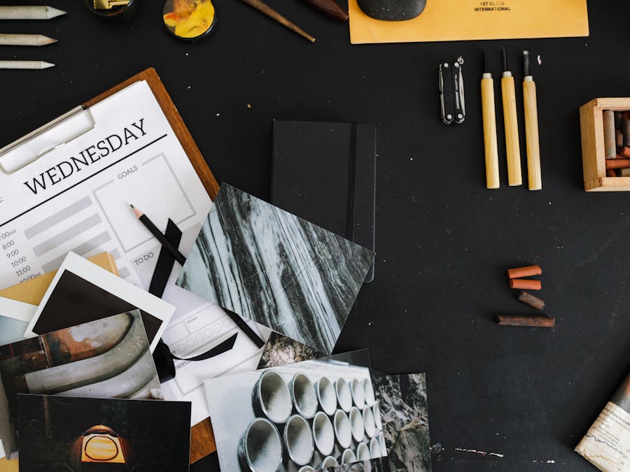 An overhead view of a creative workspace with art supplies, photographs, and a weekly planner.