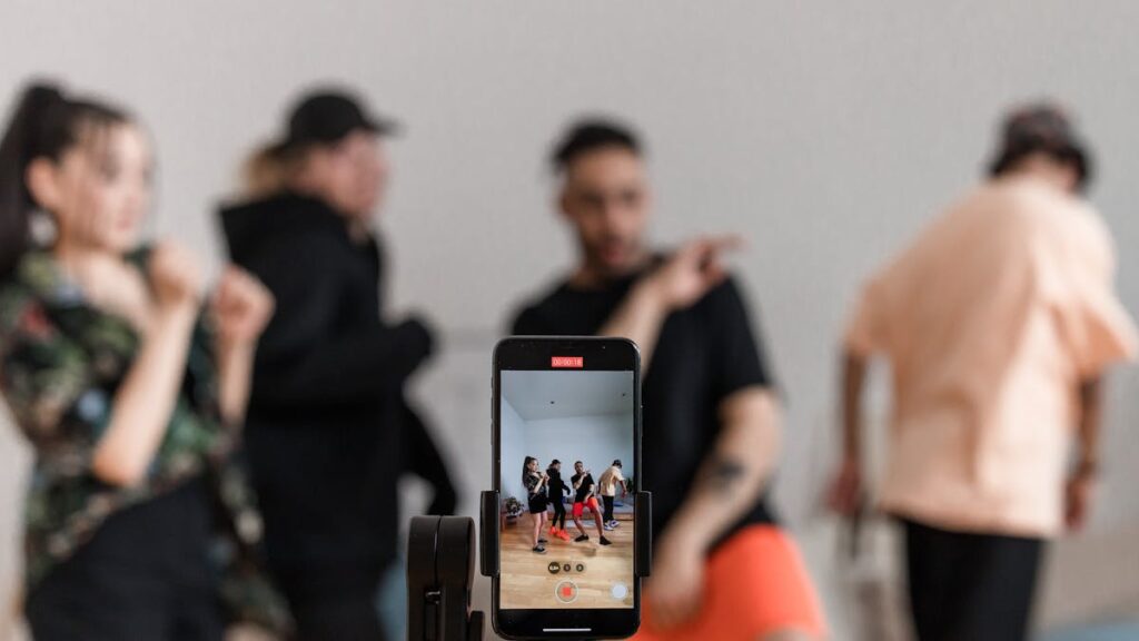 Group of dancers recording performance with smartphone on tripod, capturing trendy dance moves.