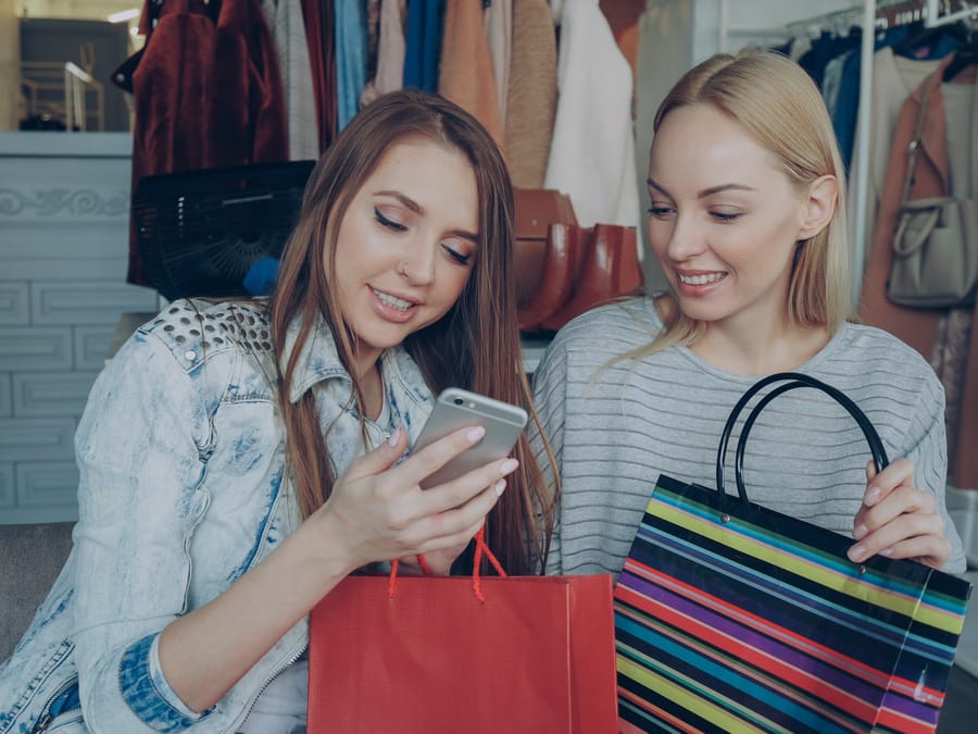 Two women enjoying shopping together, sharing content on a phone in a stylish boutique.
