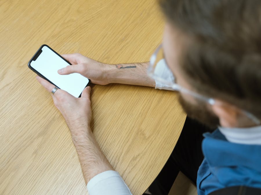 Overhead view of person holding smartphone with blank screen at a wooden table.