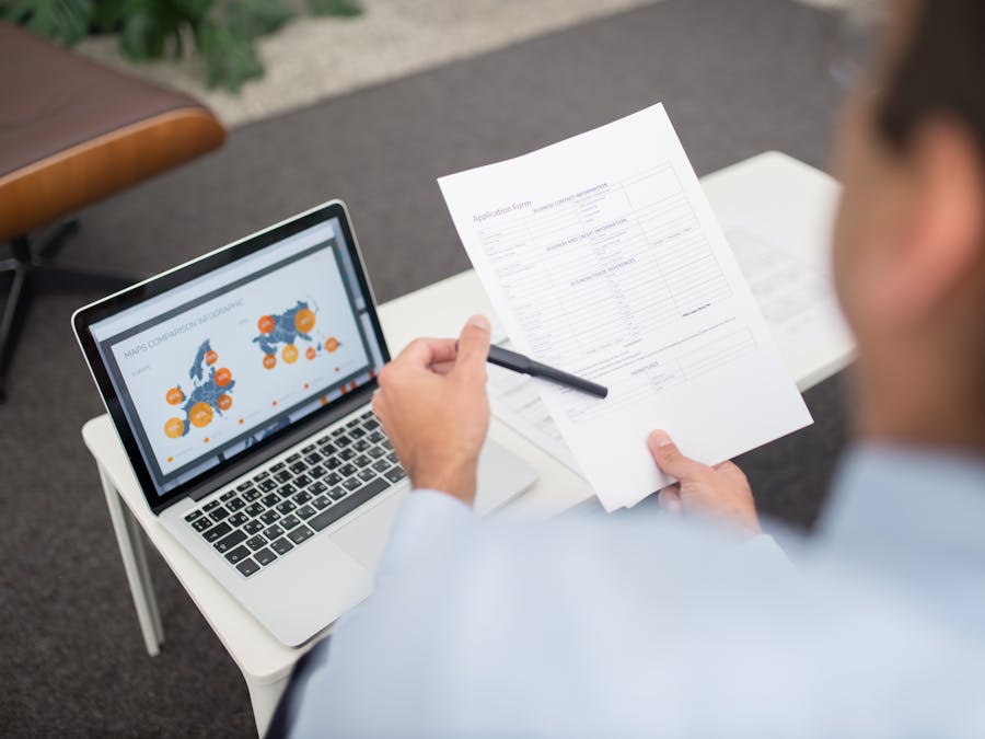 Professional setting with businessman reviewing documents and data on a laptop in an office.