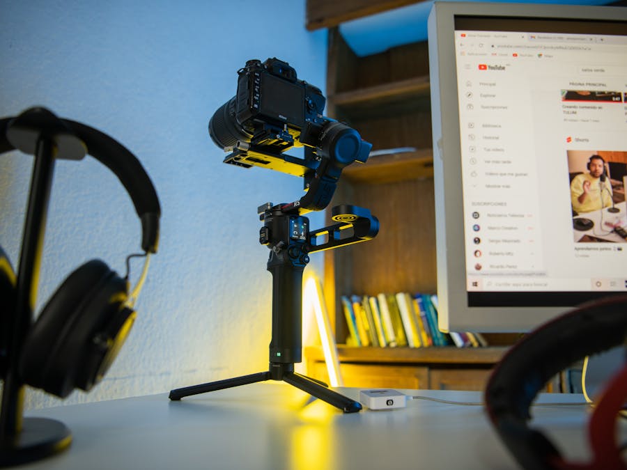 Professional photography setup featuring a camera on a tripod, headphones, and a computer monitor displaying video content.