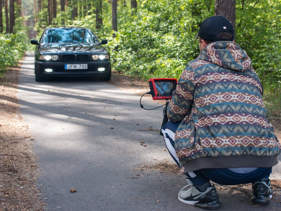 Photographer films car driving along forest road using specialized equipment.