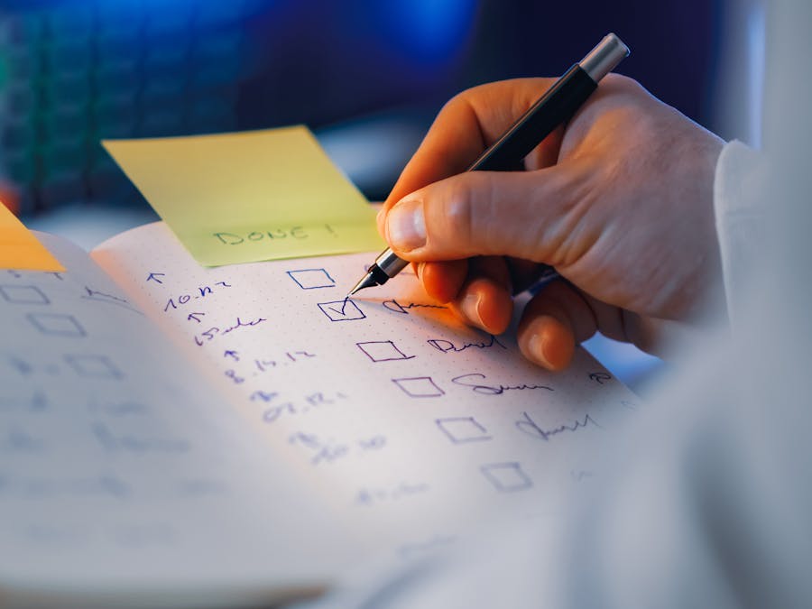 Close-up of a hand writing in a notebook with checkboxes, highlighting productivity and organization.