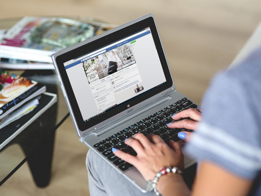 A woman typing on a laptop with social media on the screen, indoors setting.