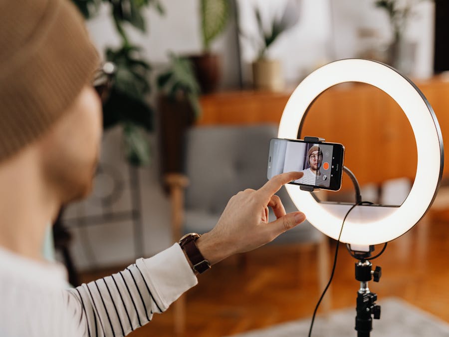 Adult male creating video content with smartphone and ring light in a cozy indoor setting.