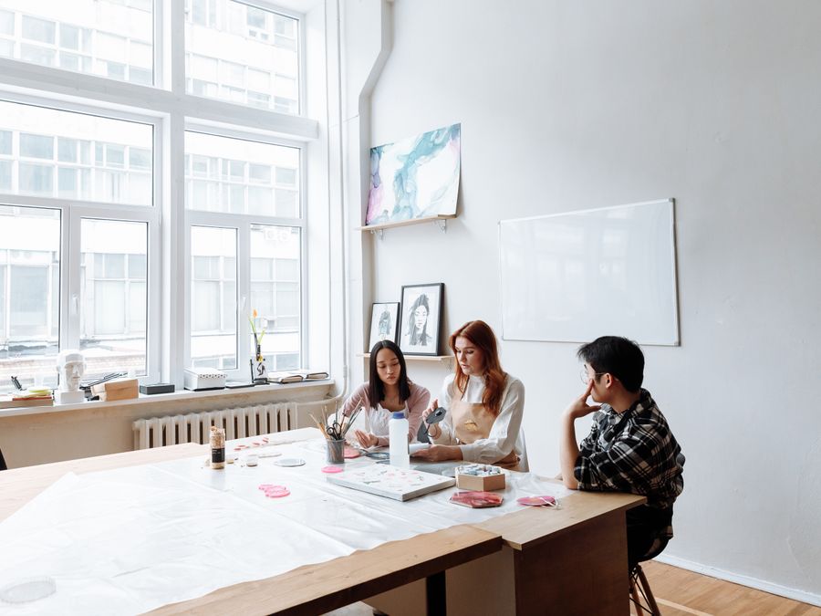 Three individuals engage in a creative art session in a modern studio with natural light.
