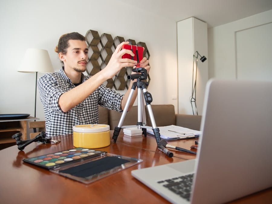 A male vlogger adjusts his camera on a tripod, preparing for a video shoot in a stylish home studio.