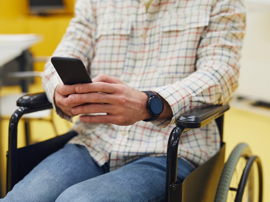 Adult using smartphone while seated in a wheelchair, wearing plaid shirt indoors.